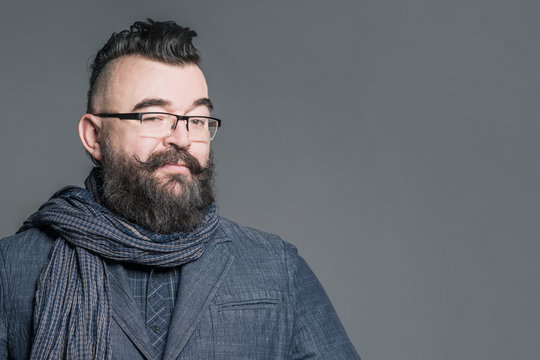 Adult bearded man in a suit, scarf, glasses and with mohawk hairstyle on a gray background