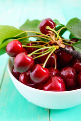 Ripe juicy red cherries in a ceramic bowl on a bright wooden background.  Vertical view