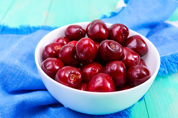Ripe juicy red cherries in a ceramic bowl on a bright wooden background.