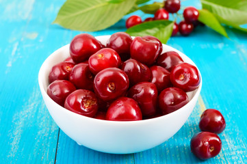 Ripe red cherry berries in a white ceramic bowl on a blue wooden background.