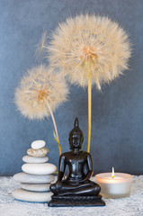 Buddha, pyramid of pebbles, burning candle and dandelion flowers as zen background