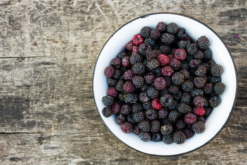Ripe blackberries in rustic bowl on old wooden background. Top view