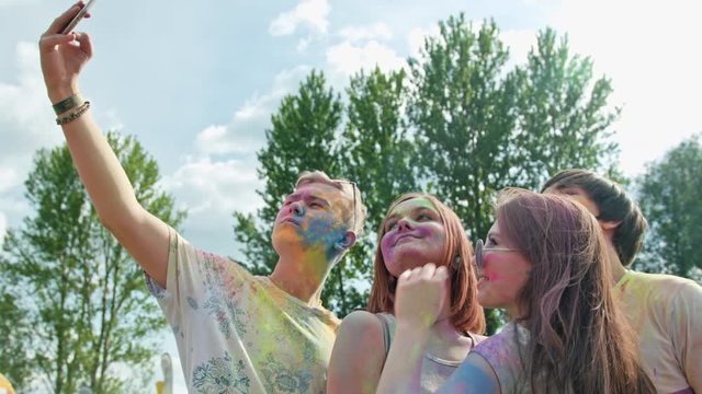 Holi festival of colors. Young people covered with powder taking a selfie. Medium shot