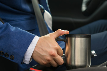 The driver in the car takes a thermos mug with a coffee bar so as not to fall asleep at the wheel
