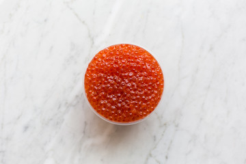 Top view of red caviar in a bowl on a light marble background