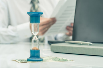 Hourglass. Businessman working in the office in the background. Concept time is money.