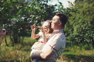 Little girl with her father playing in the Park, blowing bubbles. Happy family laughing.