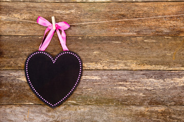 Blackboard heart with pink border and ribbon on clothespin against rustic old wooden background