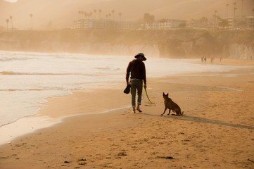 Young man and his dog on sandy beach at sundown