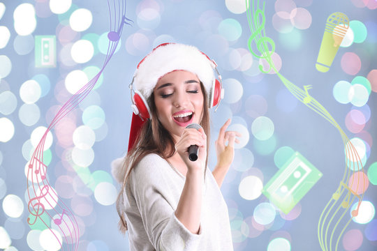 Young woman with headphones singing song on blurred lights background. Christmas and New Year music