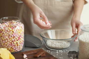 Woman adding marshmallow into glass bowl with crispy rice balls on table