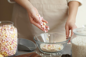 Woman adding marshmallow into glass bowl with crispy rice balls on table