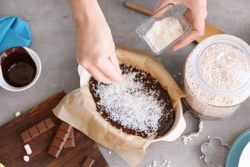 Woman sprinkling desiccated coconut onto rice dessert in baking dish on table