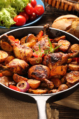 Roasted chicken legs with baked potato on frying pan