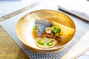 Beef tartare with quail egg is in a gold plate