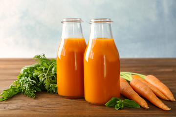 Two glass bottles of fresh juice with carrots on wooden table
