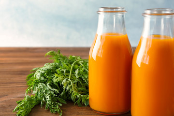 Two glass bottles of fresh carrot juice on wooden table