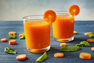 Two glasses of homemade juice with carrot slices and mint on color wooden table