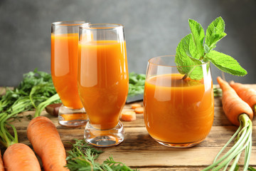 Composition with glasses of fresh carrot juice and vegetables on wooden table
