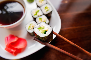 Rolls in nori seaweed with avocado, pickled ginger and soy sauce. Asian cuisine, traditional dish - sushi.
