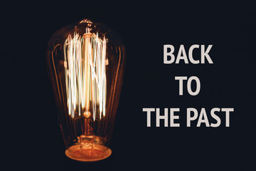 Inscription Back to the past on the image of retro bulb on a black background. The concept of time and history.