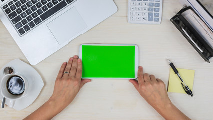 woman using a tablet PC / mobile phone  with green screen at her desk in the office - top view