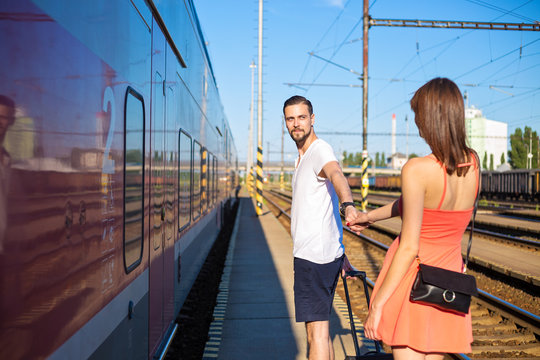 Young caucasian couple holding hands at train station, walking next to the train, wearing casual summer clothes