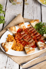 Turkish and Arabic Traditional Ramadan Iskender Adana Kofte Kebab with parsley, bulgur and cheese bread serving on rustic white wood background.