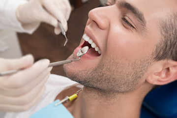 Dentist examining a patient's teeth in the dentist.Smiling man is having his teeth examined by dentist in clinic