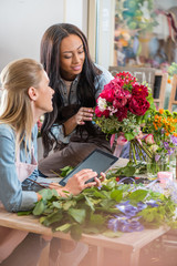 smiling young multiethnic florists working with digital tablet and flowers in flower shop