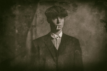 Antique wet plate photo of 1920s english gangster smoking a cigarette. Wearing suit and flat cap.