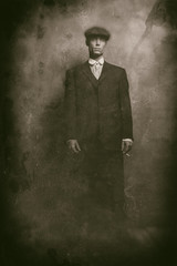 Obraz premium Antique wet plate photo of 1920s english gangster standing with cigarette. Wearing suit and flat cap.