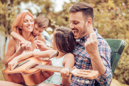 Happy young family playing guitar together and laughing