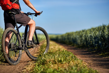 Fototapeta na wymiar Attractive one cyclist on mountainbike on path near green fields in the countryside in the summer season.