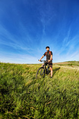 Young cyclist riding mountain bicyclist against beautiful sunset in the countryside.