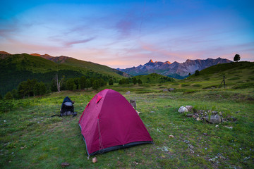 Camping with tent at high altitude on the Alps. Snowcapped mountain range and scenic colorful sky at sunset. Adventure and exploration in summertime.