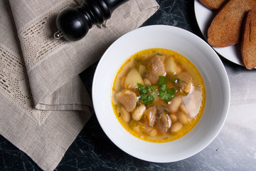 Bean soup in white plate, several toast on white plate on a black stone background.