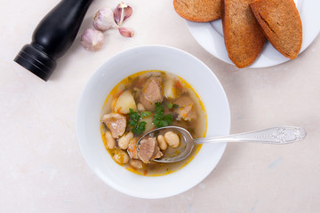 Bean soup in white plate with metal spoon, several toast on white plate on a light stone background.