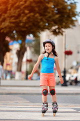 Cute little girl learning to roller skate in city skate park on beautiful summer day.