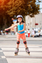 Cute little girl learning to roller skate in city skate park on beautiful summer day.