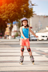 Cute little girl learning to roller skate in city skate park on beautiful summer day.