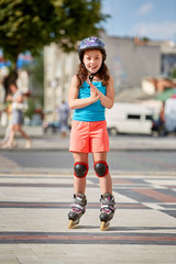 Cute little girl learning to roller skate in city skate park on beautiful summer day.
