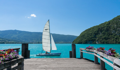 Small boat  sailing past a wooden dock on Lac d'Annecy, France.