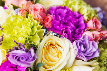 Golden wedding rings with diamonds lie inside rose flower in the bridal bouquet. Symbol of love and marriage.