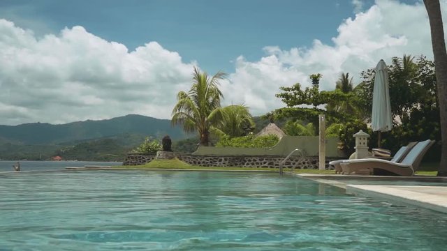 Woman in red bikini walking out of infinity swimming pool in front of ocean on a sunny summer day in Bali, Candidasa. Shot with Sony a7s on a motorized 3-axis gimbal.
