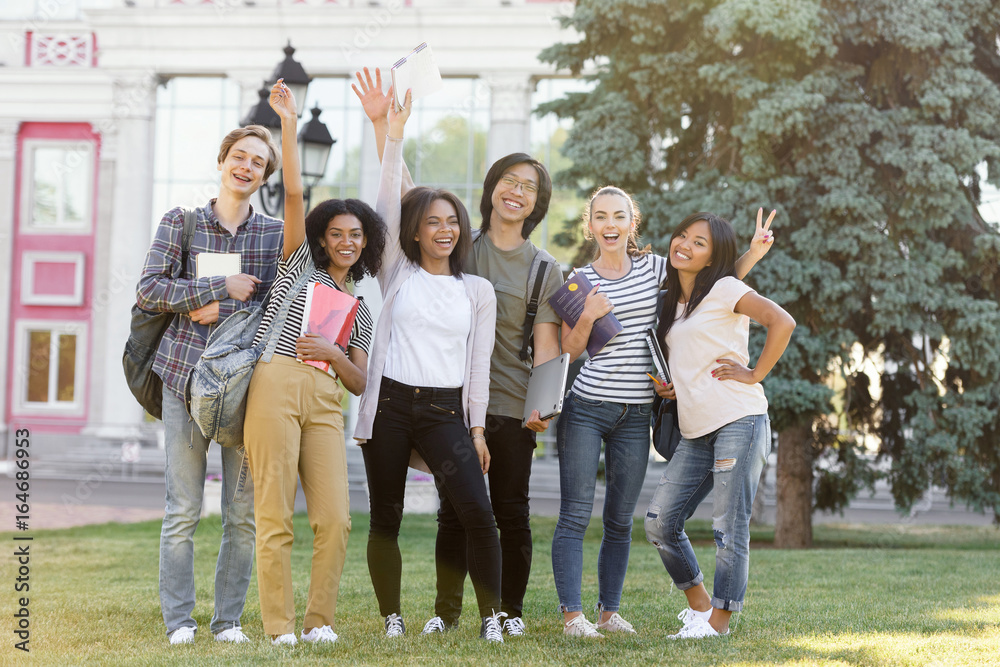 Poster young cheerful students standing outdoors waving