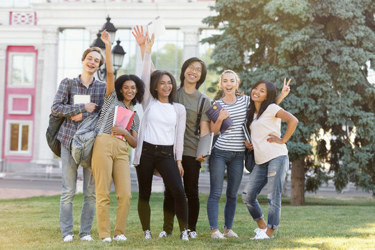 Young cheerful students standing outdoors waving