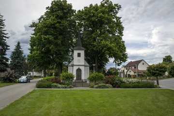 A white chapel under the large trees in the center of a small village