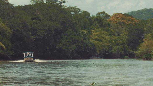 Establishing shot of a boat sailing down a river surrounded by rainforest