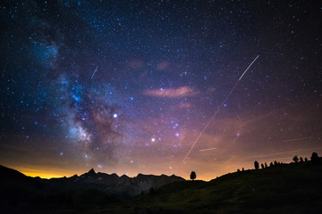 Fototapeta premium The colorful glowing core of the Milky Way and the starry sky captured at high altitude in summertime on the Italian Alps, Torino Province. Airplane traffic in the sky.